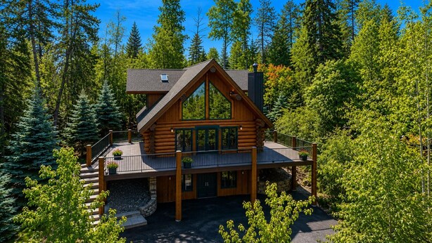 Une cabane en rondins dotée d’un balcon, entourée d’arbres.