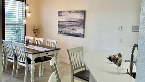 A dining area with a white table and chairs, a painting on the wall, and a kitchen counter with a sink. - Private Heated Pool & Spa Villa — 20 Min to Disney - Golf Community (Davenport)