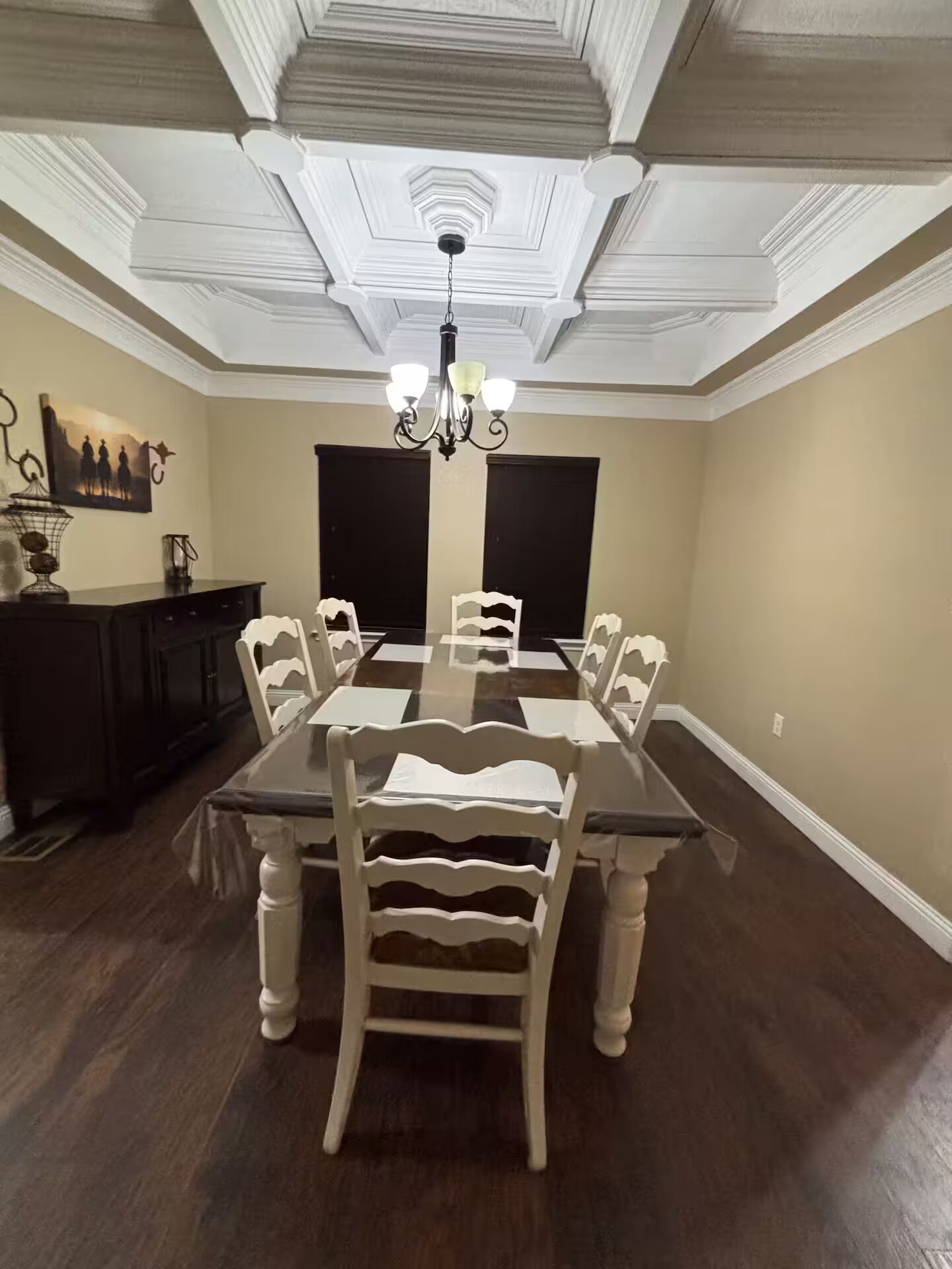 Une salle à manger avec une grande table, des chaises blanches, un lustre et un parquet en bois foncé.
