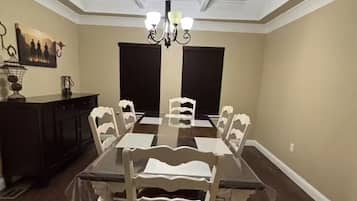 Une salle à manger avec une grande table, des chaises blanches, un lustre et un parquet en bois foncé.
