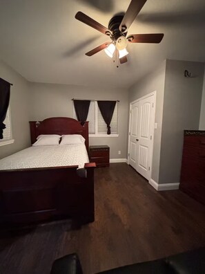 A bedroom with a wooden bed, a ceiling fan, a nightstand, a dresser, and a door. - Western Bunkhouse (Fort Worth)