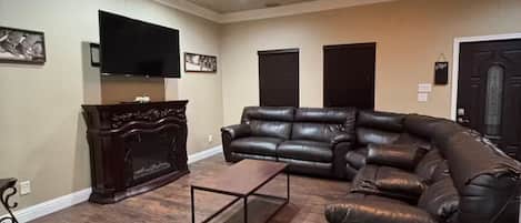 A living room with a ceiling fan, a flat-screen TV, a leather sofa, and a coffee table.
