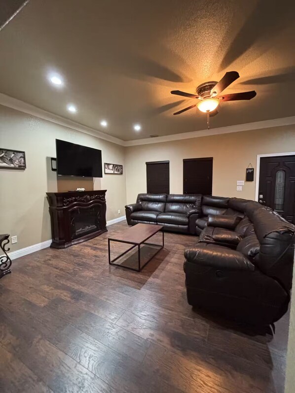 A living room with a ceiling fan, a flat-screen TV, a leather sofa, and a coffee table. - Western Bunkhouse (Fort Worth)