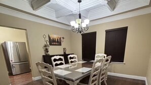 A dining area with a wooden table and chairs, a chandelier, and a view of the kitchen.