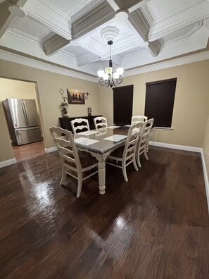 A dining area with a wooden table and chairs, a chandelier, and a view of the kitchen.