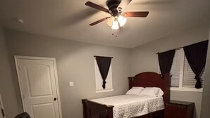 A bedroom with a single bed, a nightstand, a dresser, a ceiling fan, and a window with curtains.