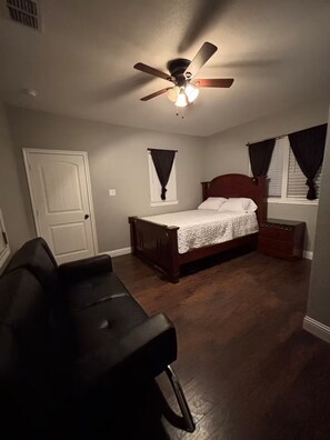 A bedroom with a single bed, a nightstand, a dresser, a ceiling fan, and a window with curtains.