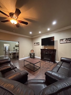 A living room with a fireplace, leather sofas, a coffee table, and a ceiling fan.