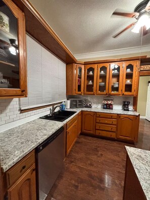 A kitchen with wooden cabinets, a dishwasher, a sink, and a ceiling fan.
