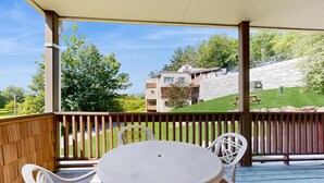 A covered outdoor area with a table and chairs, a view of a house, and a grassy slope.