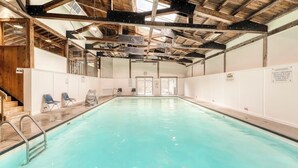 An indoor swimming pool with a wooden ceiling, white walls, and a clear view of the sky through the roof.