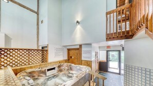 A hot tub in a room with wooden walls and a staircase.