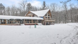Een houten hut met een groot, uitstekend dak en een balkon, omgeven door met sneeuw bedekte bomen.