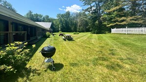 Een achtertuin met een barbecue, picknicktafels en een witte hek.