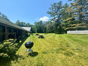 Ein Garten mit Grill, Picknicktischen und einem weißen Zaun.
