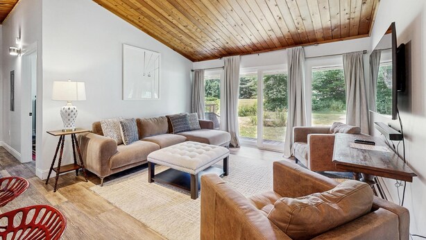 Amplia sala de estar con techo alto de madera, un conjunto de sofás, una mesa de centro, un televisor y vistas al exterior.
