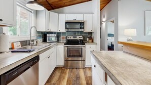 Una cocina moderna con armarios blancos, electrodomésticos de acero inoxidable y techo de madera.