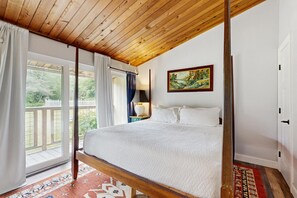 Ein Schlafzimmer mit Holzboden, einem Bett mit weißer Bettwäsche, einem Gemälde an der Wand und Blick durch das Fenster.