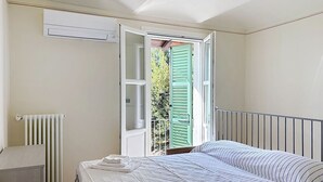 Quarto com cama, radiador e janela aberta com persianas verdes.