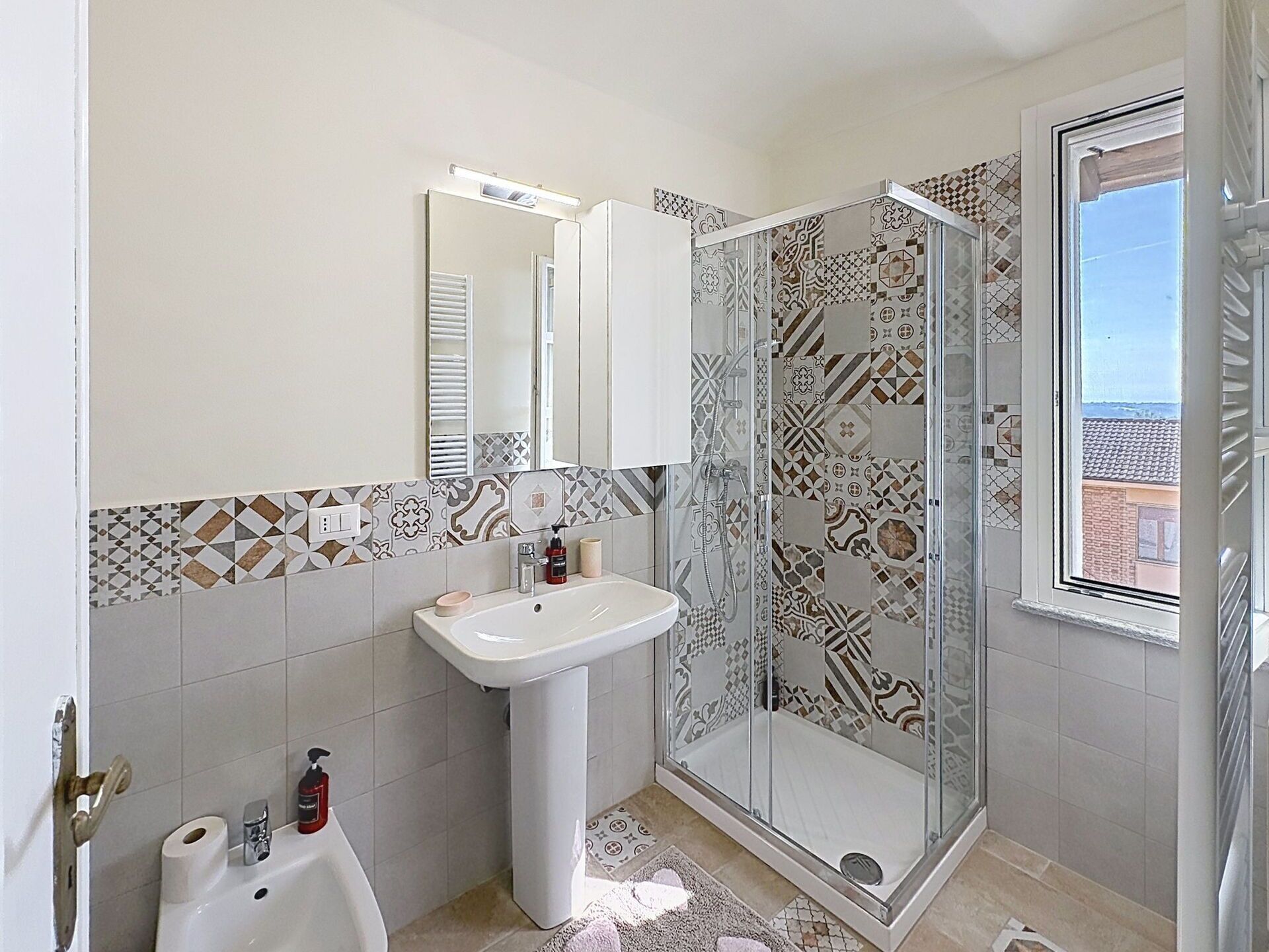 Een badkamer met een wastafel, spiegel, douche en betegelde vloer.