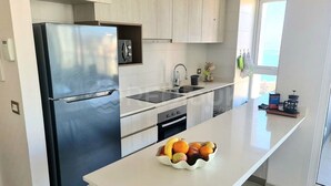 A modern kitchen with a stainless steel refrigerator, a built-in oven, a sink, and a fruit bowl on the counter. - Rbk Amplio Dpto Familiar con linda vista (Concón)