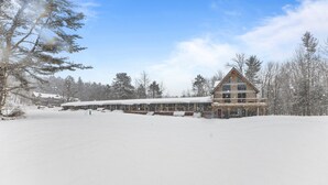 Un grand chalet doté d’un toit triangulaire imposant, d’une allée couverte et d’un paysage enneigé.