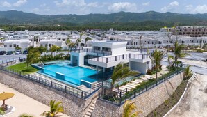 A modern hotel with a central swimming pool, surrounded by a landscaped area with palm trees. - The Vue Paradisiac Private Beach Pool Gated (St. Ann's Bay)