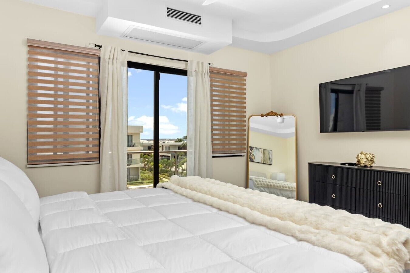 A bedroom with a large bed, a dresser, a mirror, and a TV.