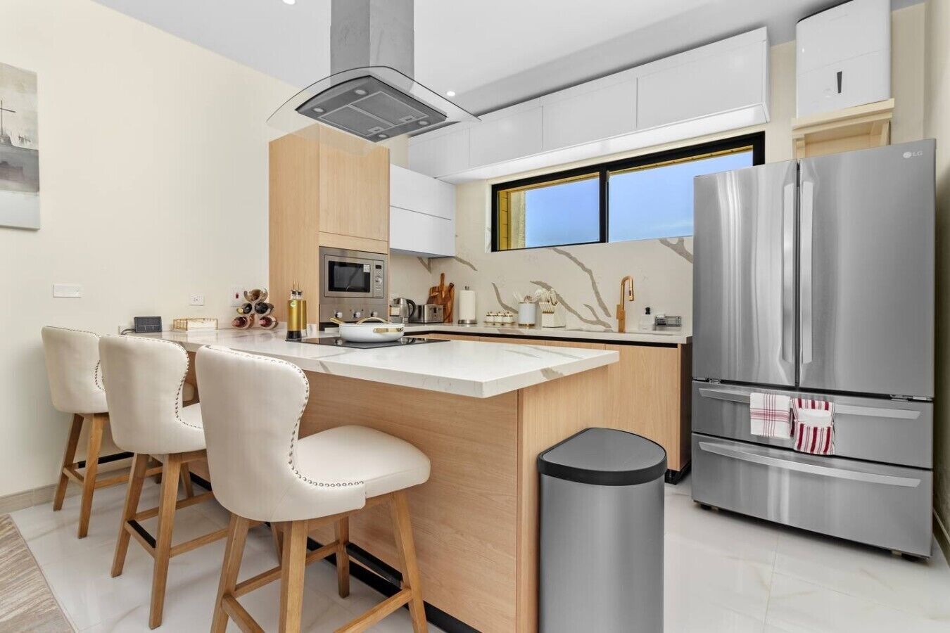 Een moderne keuken met een centraal eiland, barkrukken, een roestvrijstalen koelkast en een raam met uitzicht.