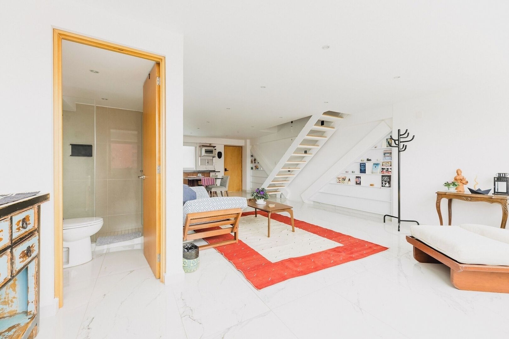 A modern loft bedroom with a bed, a desk, a staircase, and a bathroom.