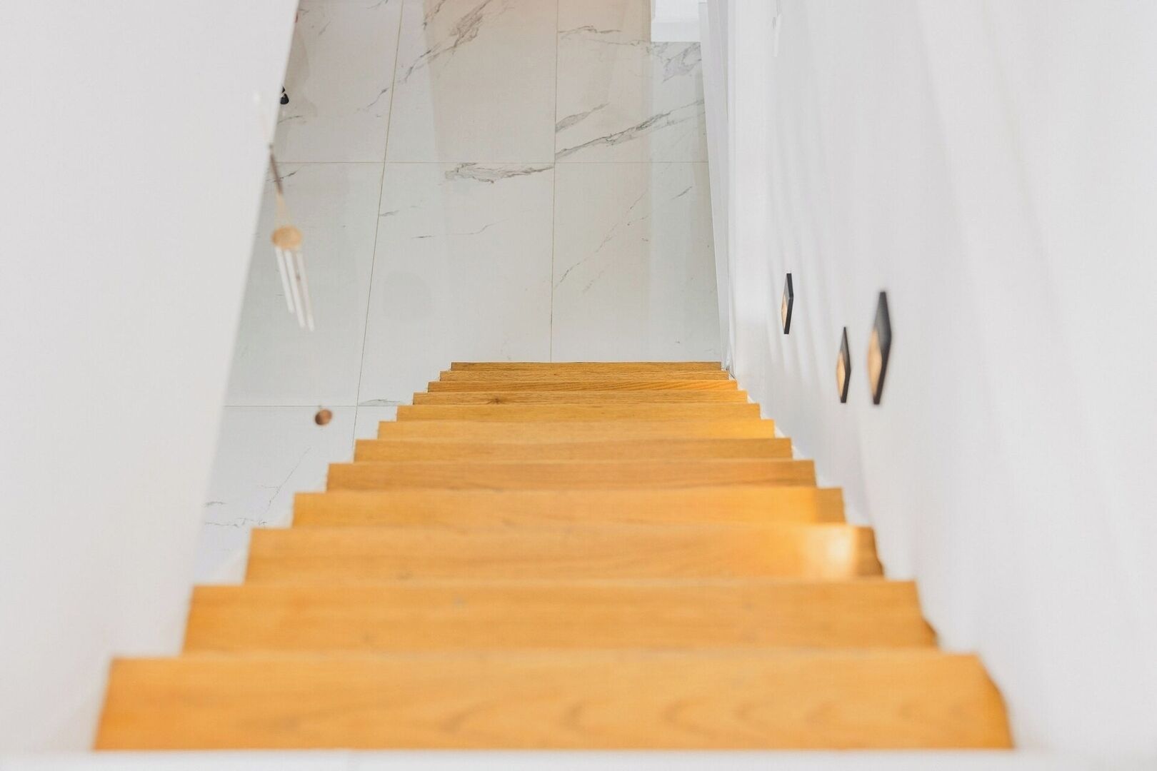 Una escalera de madera que sube a una habitación con paredes blancas y piso de mármol.