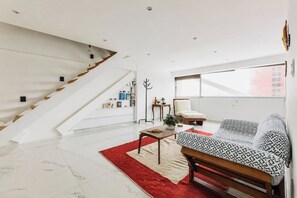 Ein modernes Wohnzimmer mit Treppe, einer Couch, einem Couchtisch und einem großen Fenster.