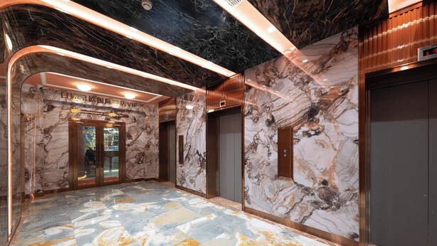 Un hall d’entrée au sol en marbre, avec un comptoir d’accueil, des ascenseurs et un panneau indiquant un espace réservé aux personnalités importantes.