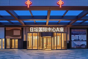 A hotel entrance with a glass facade, a revolving door, and a sign with Chinese characters. - Beijing Panoramic European Manor Hotel (Beijing)