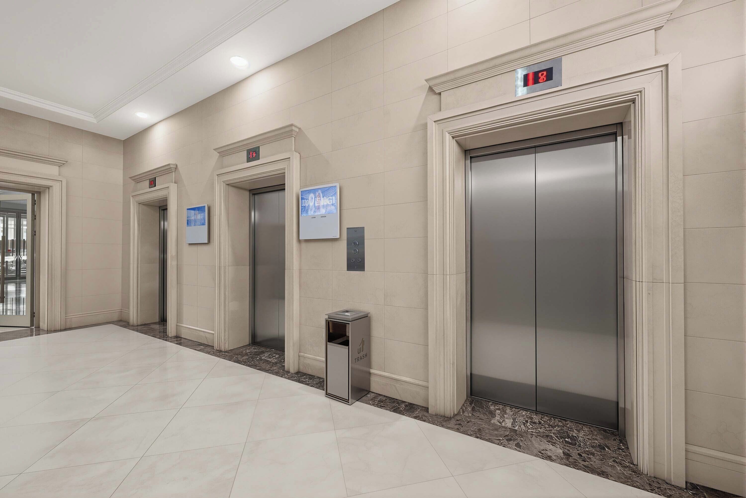 A clean, modern elevator area with three elevators, a trash bin, and a digital clock.