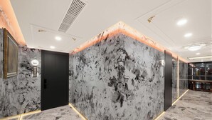 Un couloir aux murs de marbre, une porte noire et une enseigne circulaire illuminée.