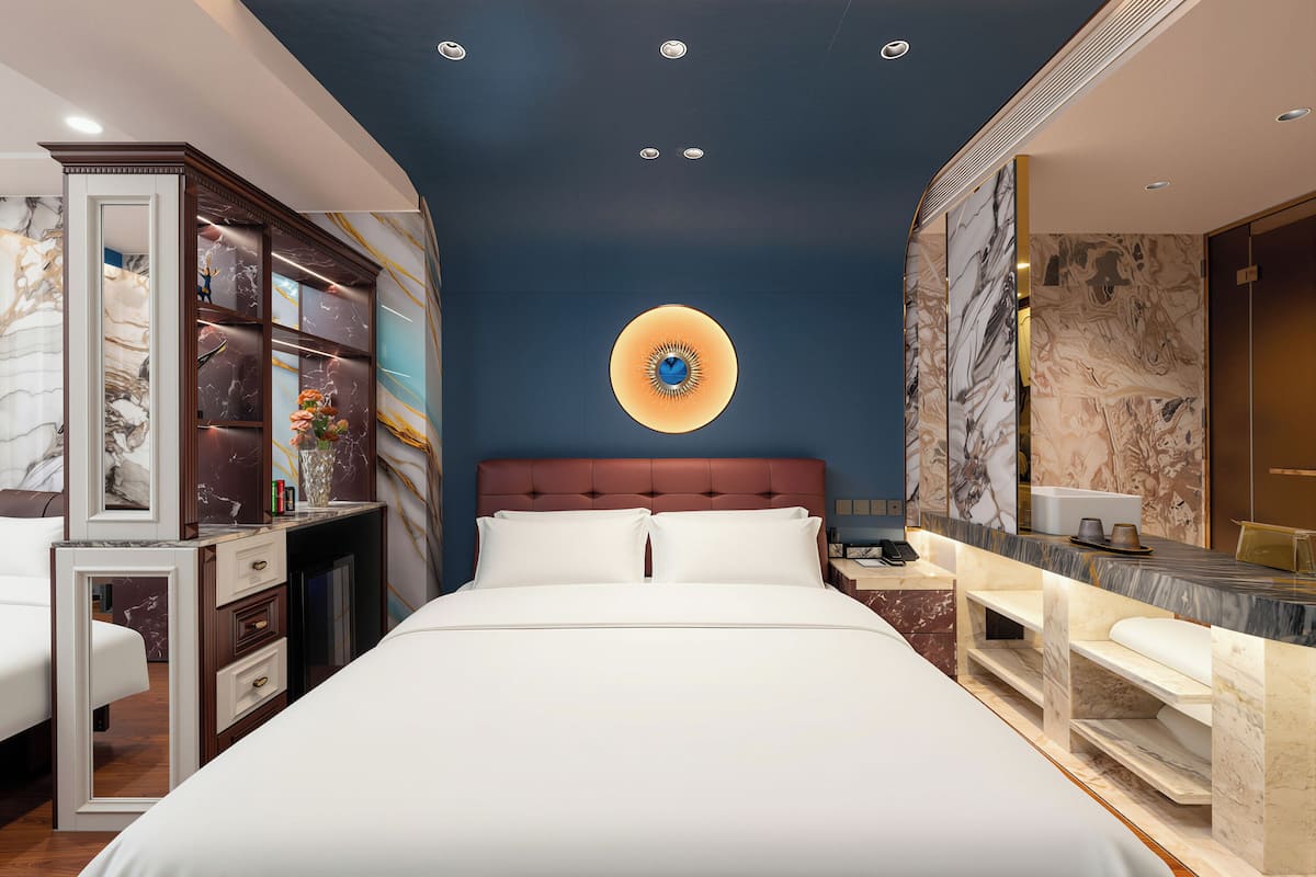 A modern hotel room with a large bed, a desk, and a vanity with a marble countertop.
