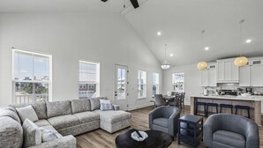 A spacious living area with a sectional sofa, a round table, and a kitchen with white cabinets and a bar area. - Short walk to beach/quiet community (Galveston)