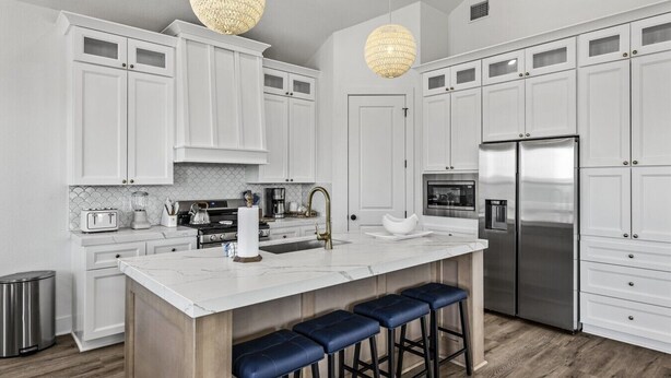 A modern kitchen with white cabinetry, a central island with bar stools, stainless steel appliances, and pendant lighting. - Short walk to beach/quiet community (Galveston)