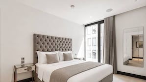 Ein modernes Hotelzimmer mit einem großen Bett, einem Nachttisch, einem Spiegel und einem Fenster mit Vorhängen.