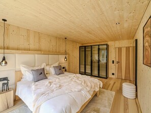 Ein modernes Schlafzimmer mit Holzboden, einem großen Bett mit weißer Bettwäsche und einem Glastaktschrank.