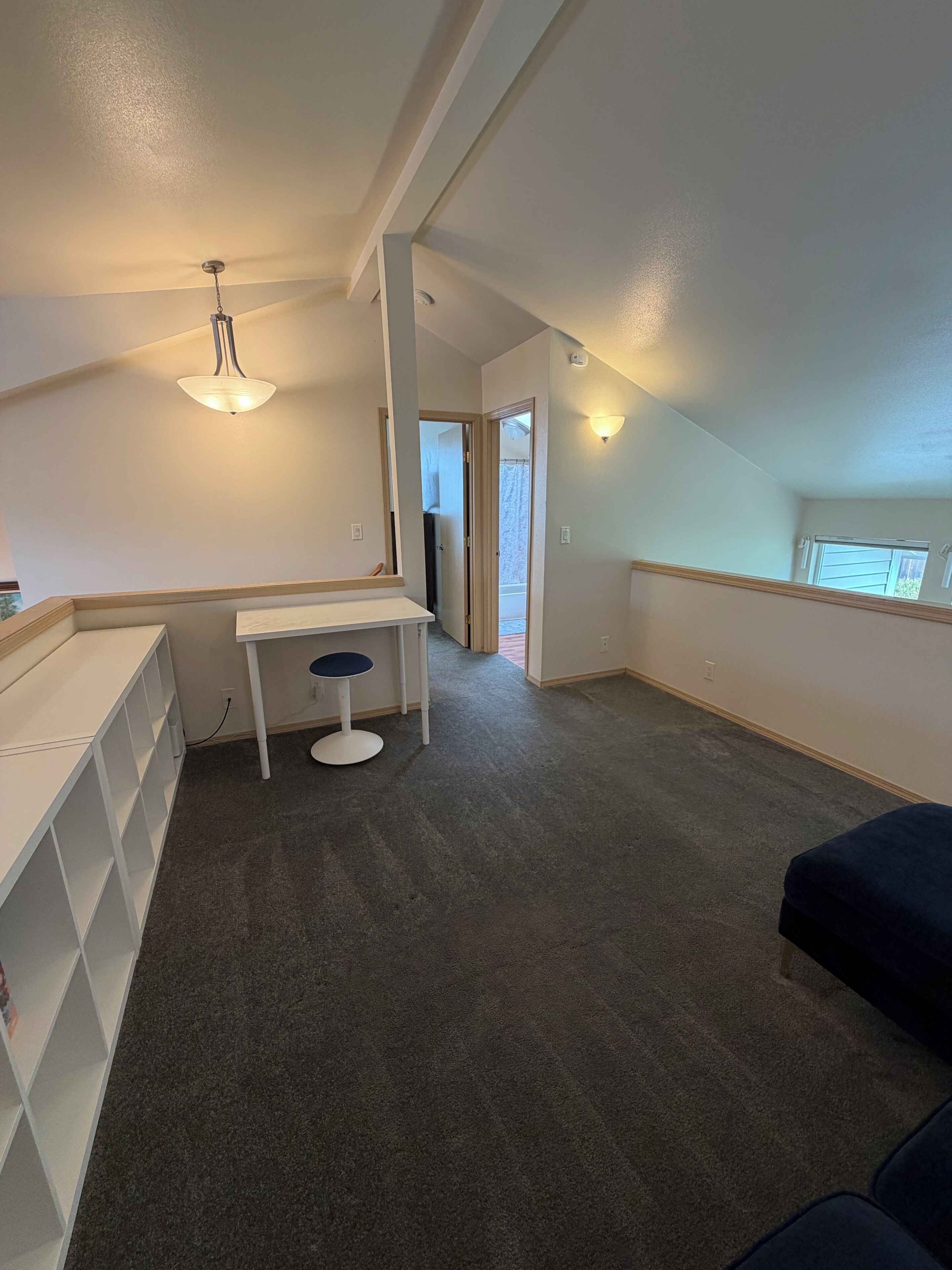 A room with a desk, chair, and shelving unit. There is a door leading to another room.