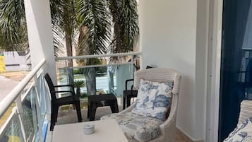 Uma varanda com móveis de vime, uma mesa branca e vista para palmeiras.