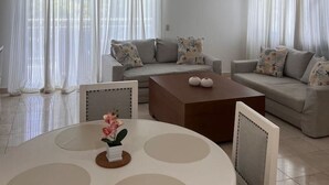 A living room with a ceiling fan, two sofas with patterned cushions, a round coffee table, and a small table with a vase of flowers. - Beach Condo 2 Pools Walk to Beach Bars Eats (Punta Cana)