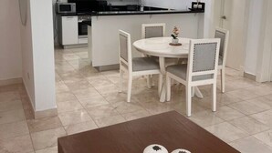 A modern kitchen with white cabinetry, a dining area with a round table and chairs, and a brown coffee table with decorative items. - Beach Condo 2 Pools Walk to Beach Bars Eats (Punta Cana)