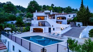 Une villa à plusieurs étages dotée d’une piscine, d’un espace salon extérieur et d’un escalier menant à une terrasse.