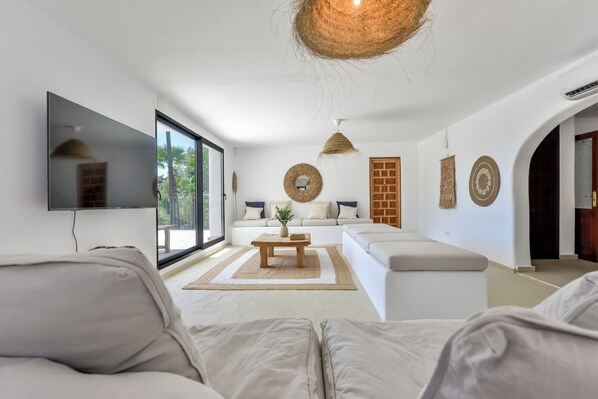 A modern living room with a sofa, a coffee table, and a TV mounted on the wall. - Finca CampoMar - By Almarina Villas (BENISSA)