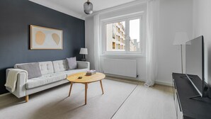 Ein modernes Wohnzimmer mit einer Couch, einem runden Couchtisch, einer TV-Bank und einem Fenster mit Blick auf Gebäude.