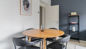 Ein moderner Essbereich mit einem runden Tisch, schwarzen Stühlen, einem gerahmten abstrakten Kunstwerk und einer Bücherwand mit Büchern und einer Vase.