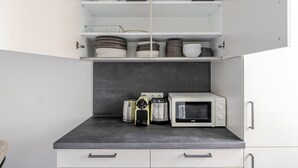 Eine Küche mit Mikrowelle, Kaffeemaschine und Kaffeemühle auf der Arbeitsplatte. Darüber befinden sich Schränke mit Geschirr und Schüsseln.